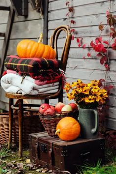 a stack of blankets, pumpkins and other autumn decorations on an old chair in front of a house