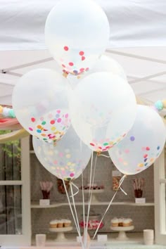 white balloons with confetti on them in front of a cake table