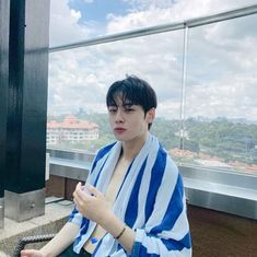 a young man sitting on top of a building next to a metal pole and wearing a blue and white striped towel