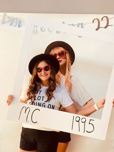 two young women are holding up a sign that reads mc195, and one is wearing a hat