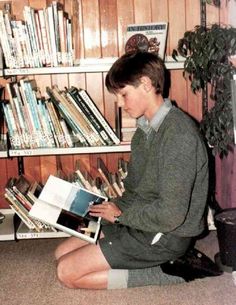 a young man sitting on the floor in front of a bookshelf reading a book