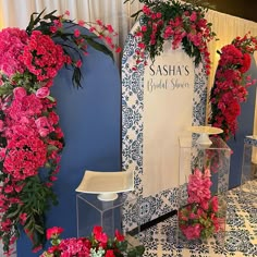 pink flowers and greenery are on display in front of a blue wall with white curtains