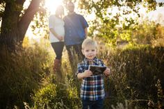 a little boy standing in the grass with his parents behind him and holding an object