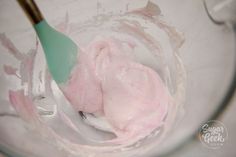 a spoon in a glass bowl filled with pink icing