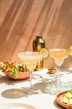 two martini glasses with limes and an avocado on the side sitting on a table