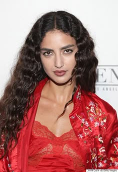 a woman with long dark hair wearing a red robe and posing for the camera in front of a white background