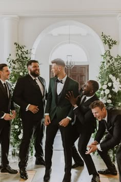 four men in tuxedos are laughing and posing for the camera while another man looks on