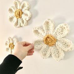 two crocheted flowers being held by someone's hand on a white surface