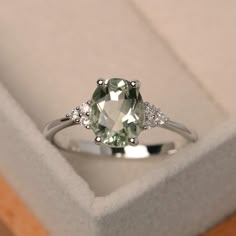 an engagement ring in a box with a green and white stone on the front, surrounded by diamonds