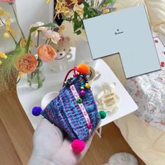 a person holding a small purse in front of a table with flowers and other items on it