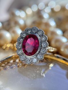 a close up of a ring with a red stone surrounded by pearls and other jewelry