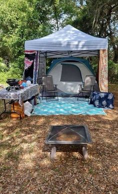 a tent is set up in the woods with chairs and tables around it, next to an open fire pit