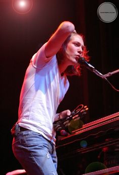 a woman standing in front of a keyboard on stage with her hand up to the microphone