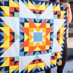 a woman holding up a colorful quilt on the street