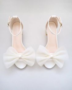 a pair of white high heeled shoes with a bow