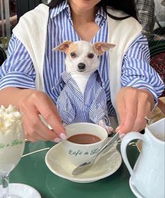 a woman sitting at a table with a cup of coffee and a small dog in her lap