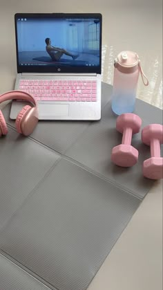 an open laptop computer sitting on top of a table next to pink dumbs and headphones