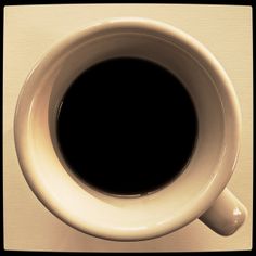 a cup of coffee sitting on top of a white counter next to a black object