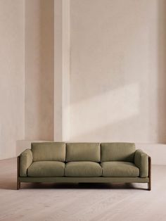 a green couch sitting on top of a hard wood floor next to a white wall