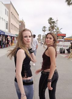 two young women standing next to each other on a street with palm trees in the background