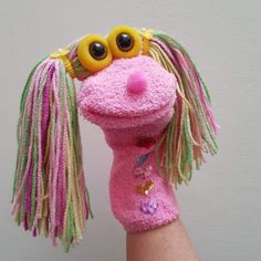 a hand holding a pink stuffed animal with yellow eyes