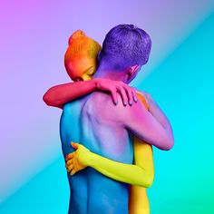 two people hugging each other with colored paint on their body and arms, in front of a multi - colored background