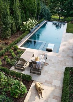 a person sitting on a chair next to a swimming pool with a dog laying in the yard