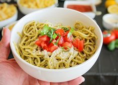 a person holding a bowl of pasta with tomatoes and cheese