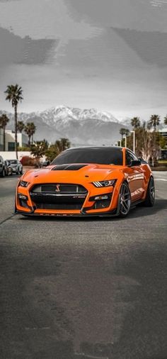 an orange sports car parked in a parking lot with palm trees and mountains in the background