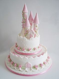 a three tiered cake decorated with pink and white icing, roses and castle decorations