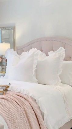 a bed with white linens and pillows in a bedroom next to a mirror on the wall