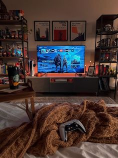 a living room with a large screen tv and game controllers on the bed in front of it