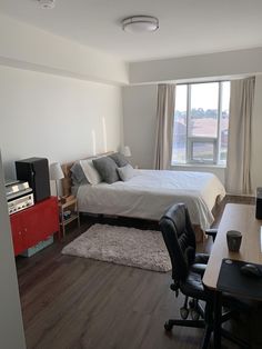 a bedroom with a bed, desk and television in it's corner area next to a window