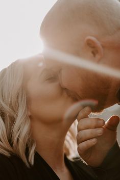 a man and woman kissing each other in front of the sun shining down on them