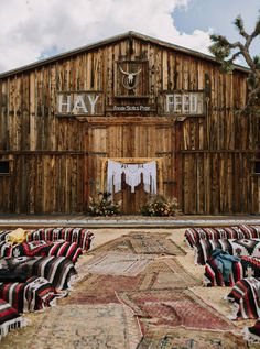 an old barn with lots of chairs and rugs on the ground in front of it