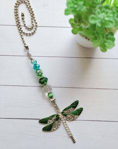 a green dragonfly necklace on a white table next to a potted plant