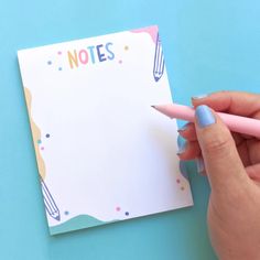 a person holding a pink pen and writing on a notepad with the word notes