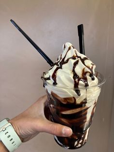 a hand holding up a chocolate milkshake with whipped cream and chocolate syrup on top