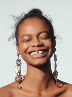 a woman smiling with her eyes closed wearing earrings