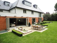 an outdoor living room and dining area in a large backyard with grass, shrubs and lawn furniture