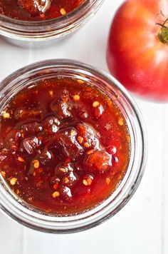 two jars filled with tomato sauce next to an apple on a white counter top,