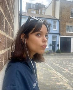 a woman wearing headphones leaning against a brick wall