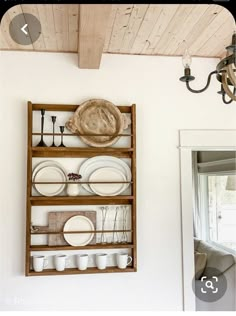 a shelf filled with dishes and plates on top of a white wall next to a mirror