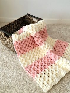 a pink and white crocheted blanket sitting on the floor next to a basket