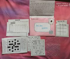 several pieces of paper with crosswords on them sitting on top of a pink blanket