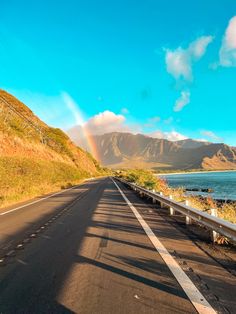 a rainbow is seen in the distance over an empty road by the ocean and mountains