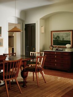 a dining room table and chairs in front of a doorway with a painting on the wall