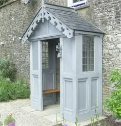 a small gray building sitting in the middle of a garden