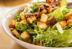 a salad with croutons and lettuce in a white bowl on a table