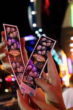 two people holding up photos in front of the camera at night with neon lights behind them